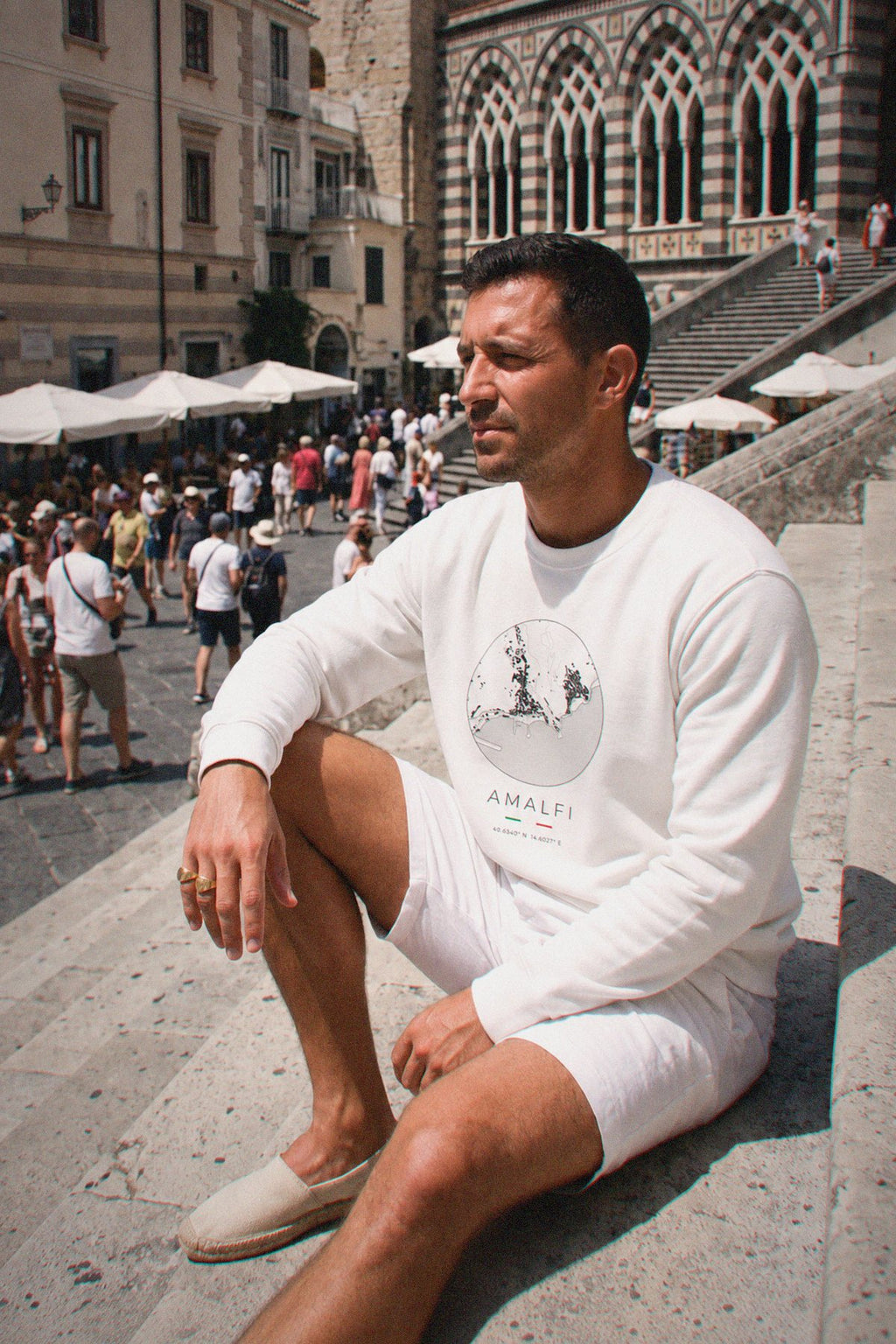 A man wearing the white crewneck sweatshirt carrying the real street map of Amalfi as a circle, photographed in Amalfi