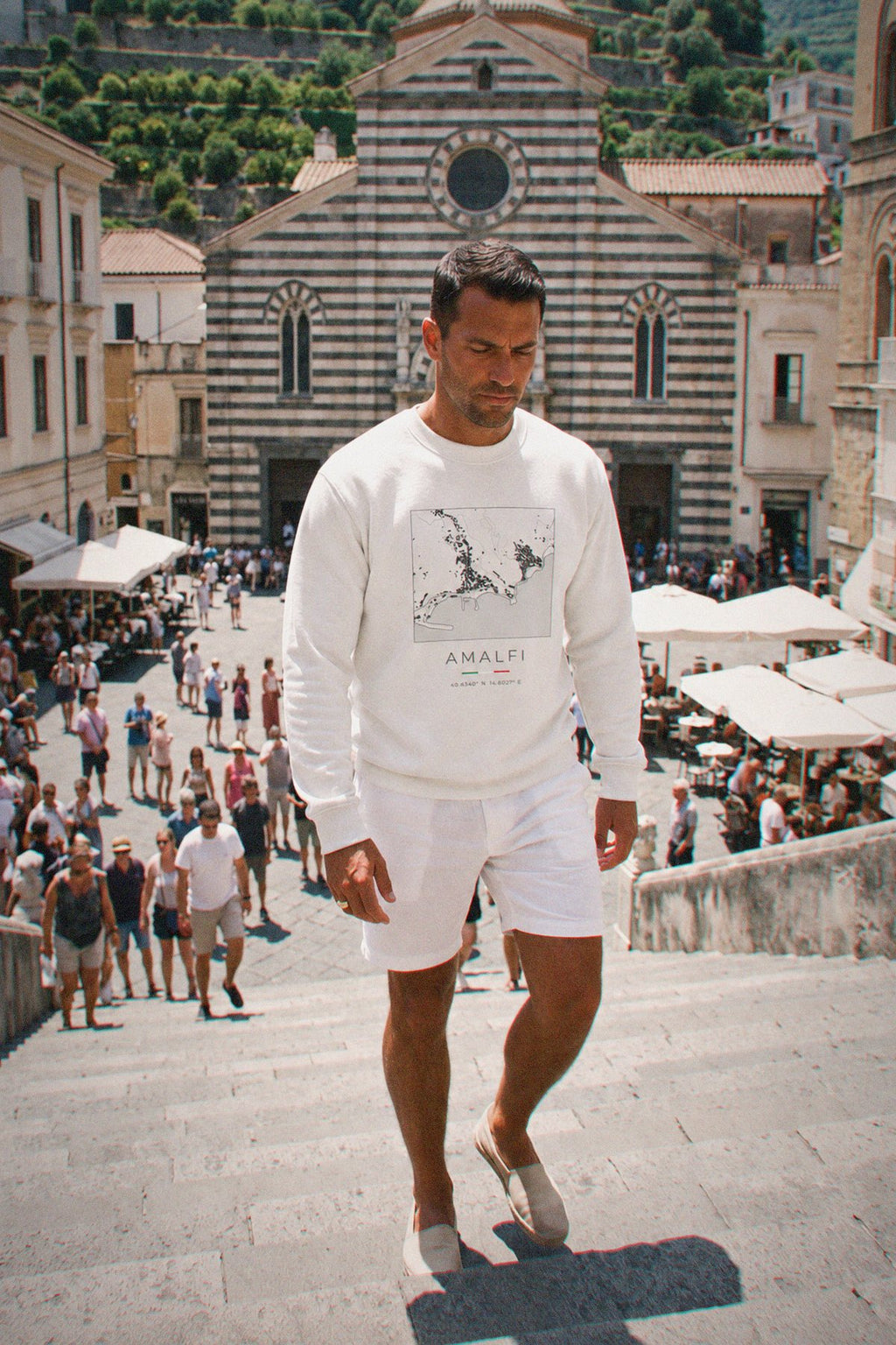 A man wearing the white crewneck sweatshirt carrying the real street map of Amalfi as a square, photographed in Amalfi