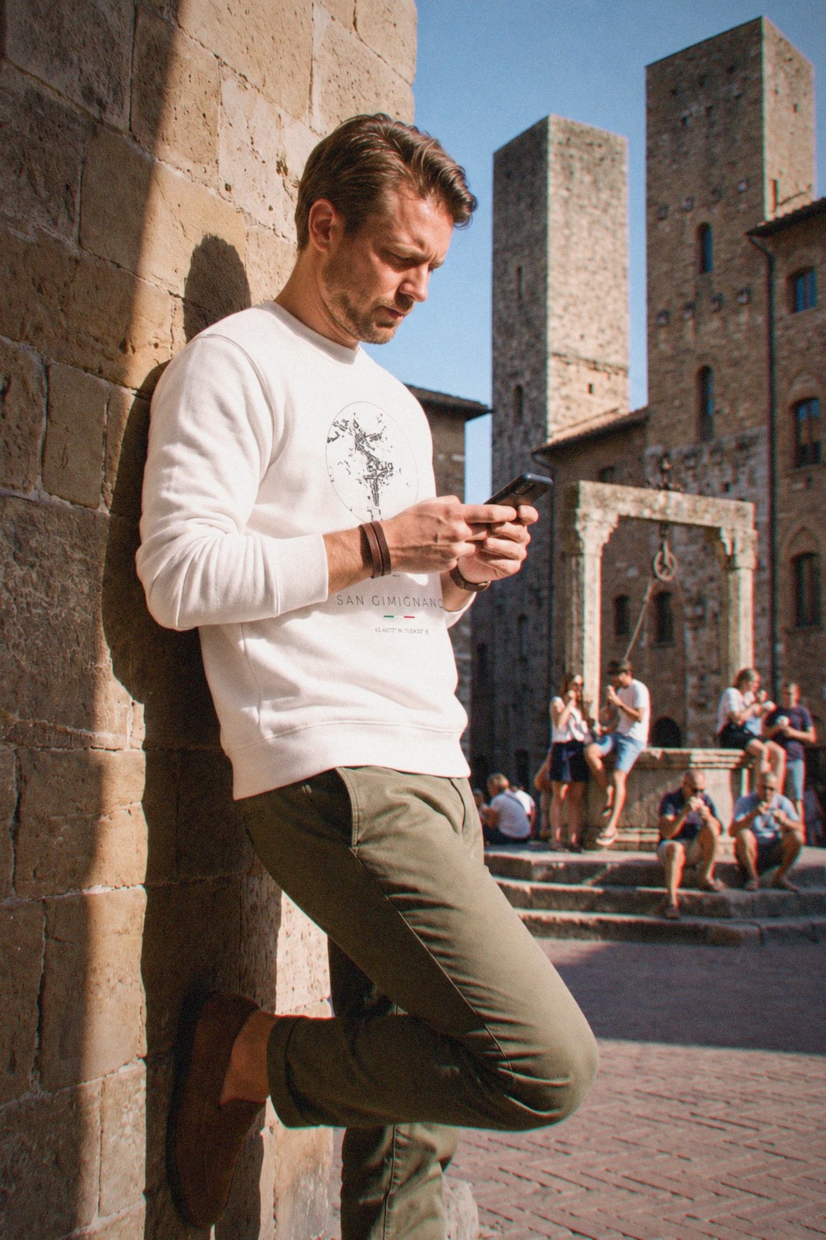 A man wearing the white crewneck sweatshirt carrying the real street map of San Gimignano as a circle, photographed in San Gimignano