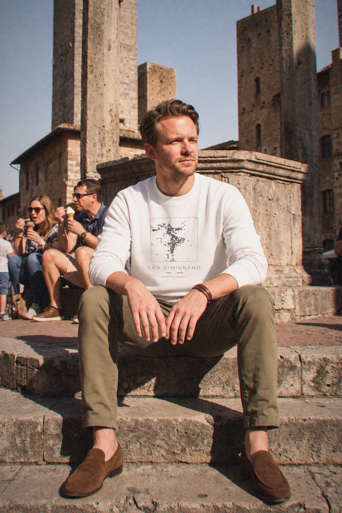 A man wearing the white crewneck sweatshirt carrying the real street map of San Gimignano as a square, photographed in San Gimignano